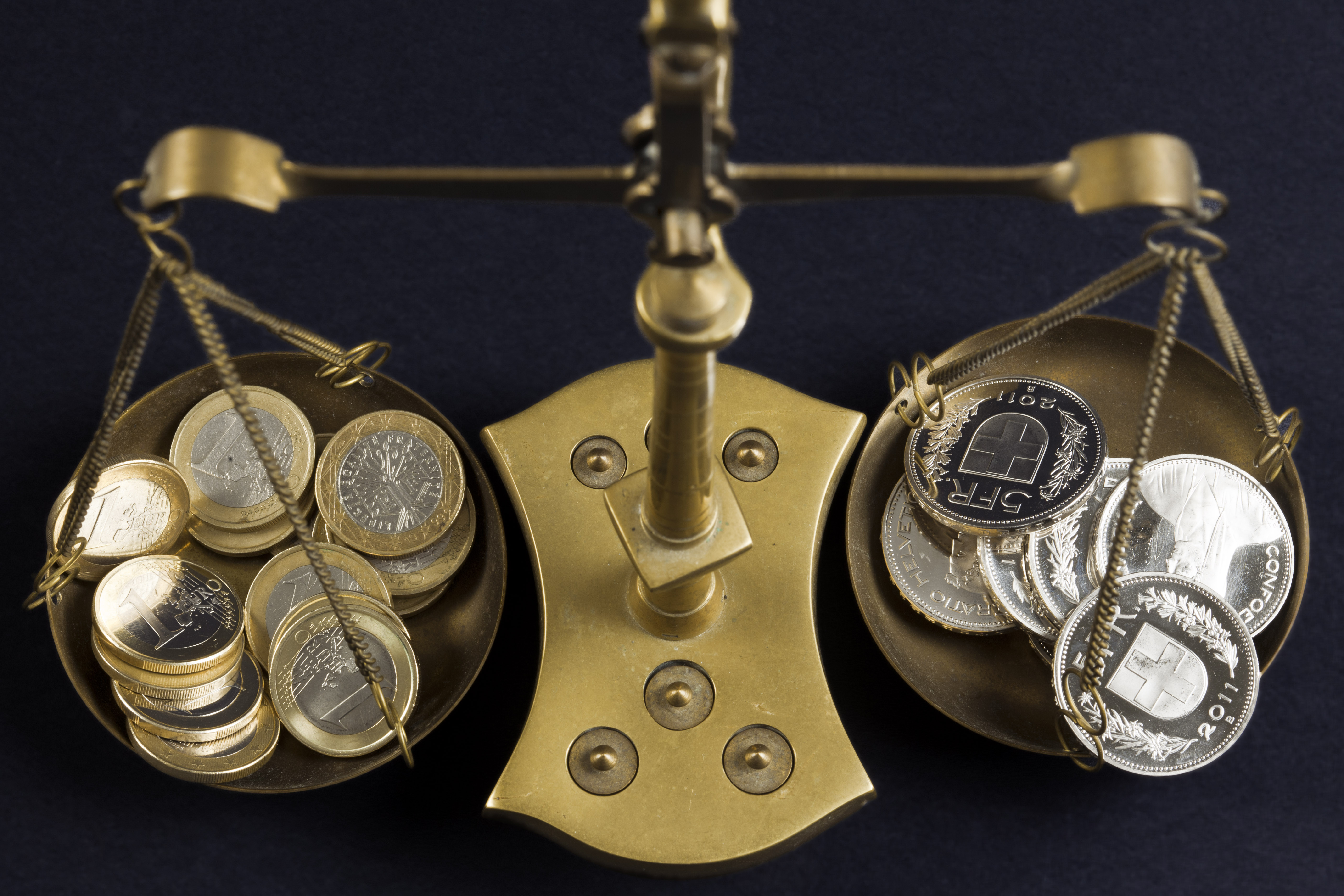 Una bilancia con da un lato moneta di euro e dall'altro monete svizzere.