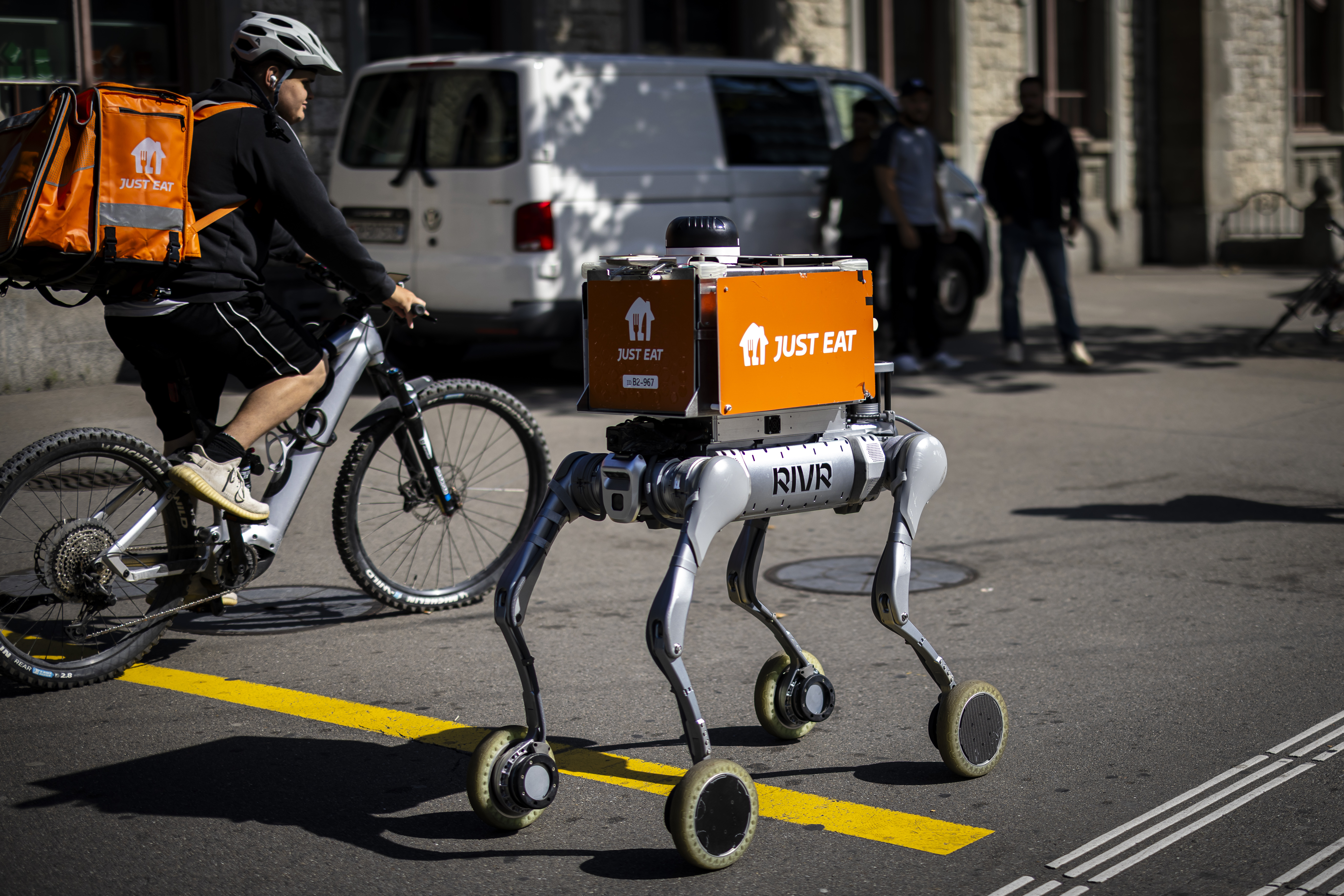 Ein Bodenroboter mit Aufschrift «Just Eat», unterwegs neben einem «Just Eat»-Fahrradkurier