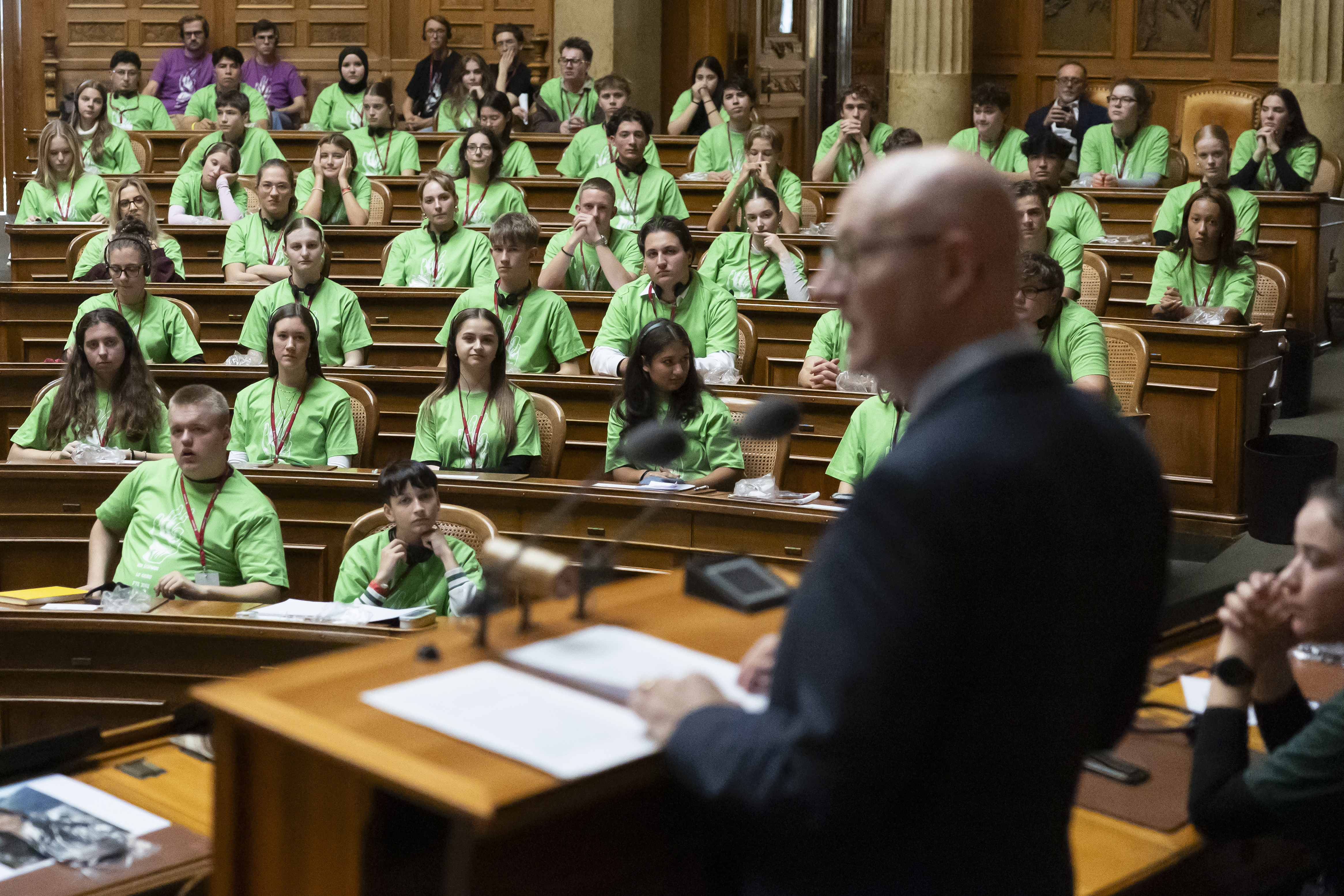 un uomo parla a una platea di giovani nella sala di un parlamento