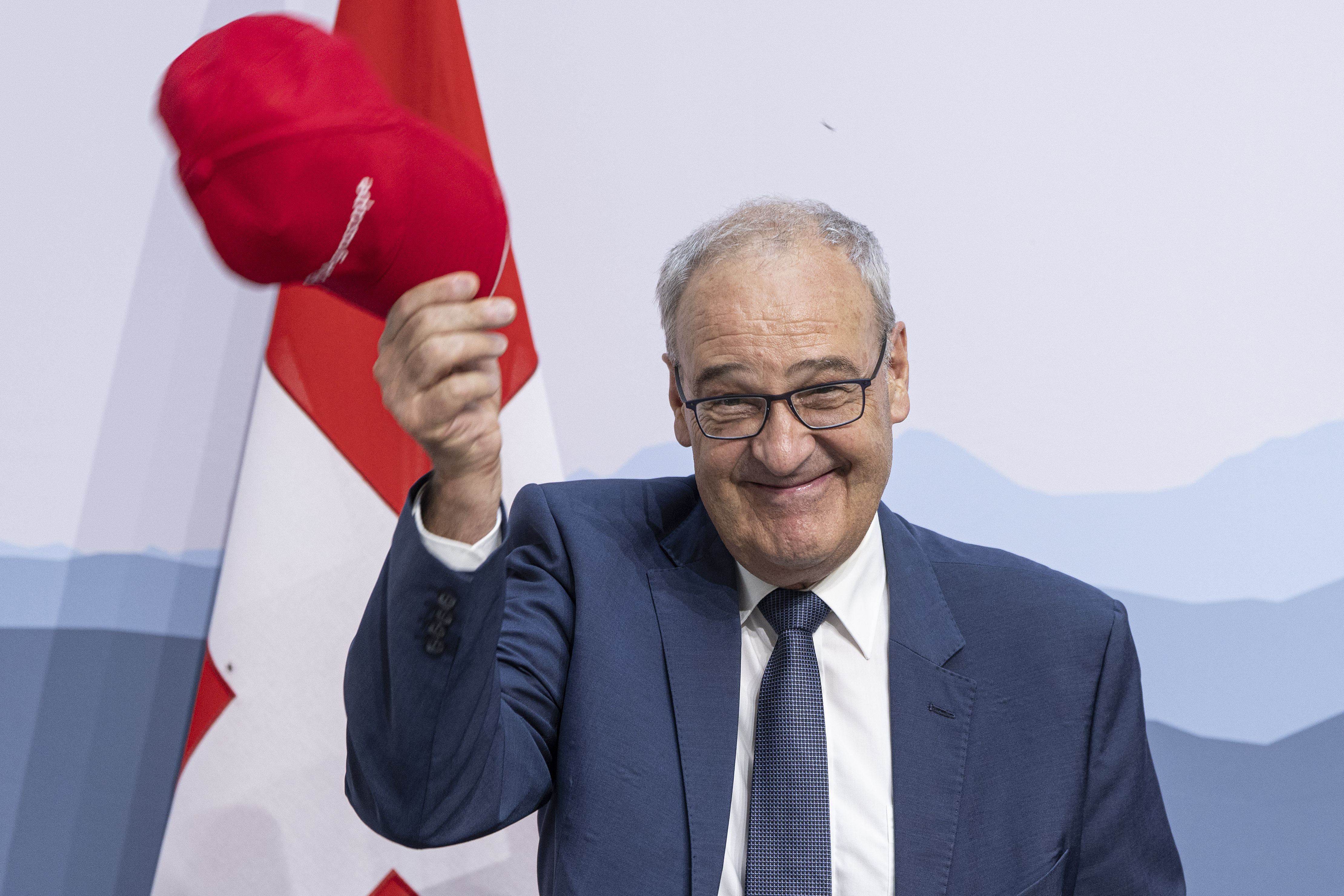 un uomo sorride mentre tiene in mano un cappellino rosso