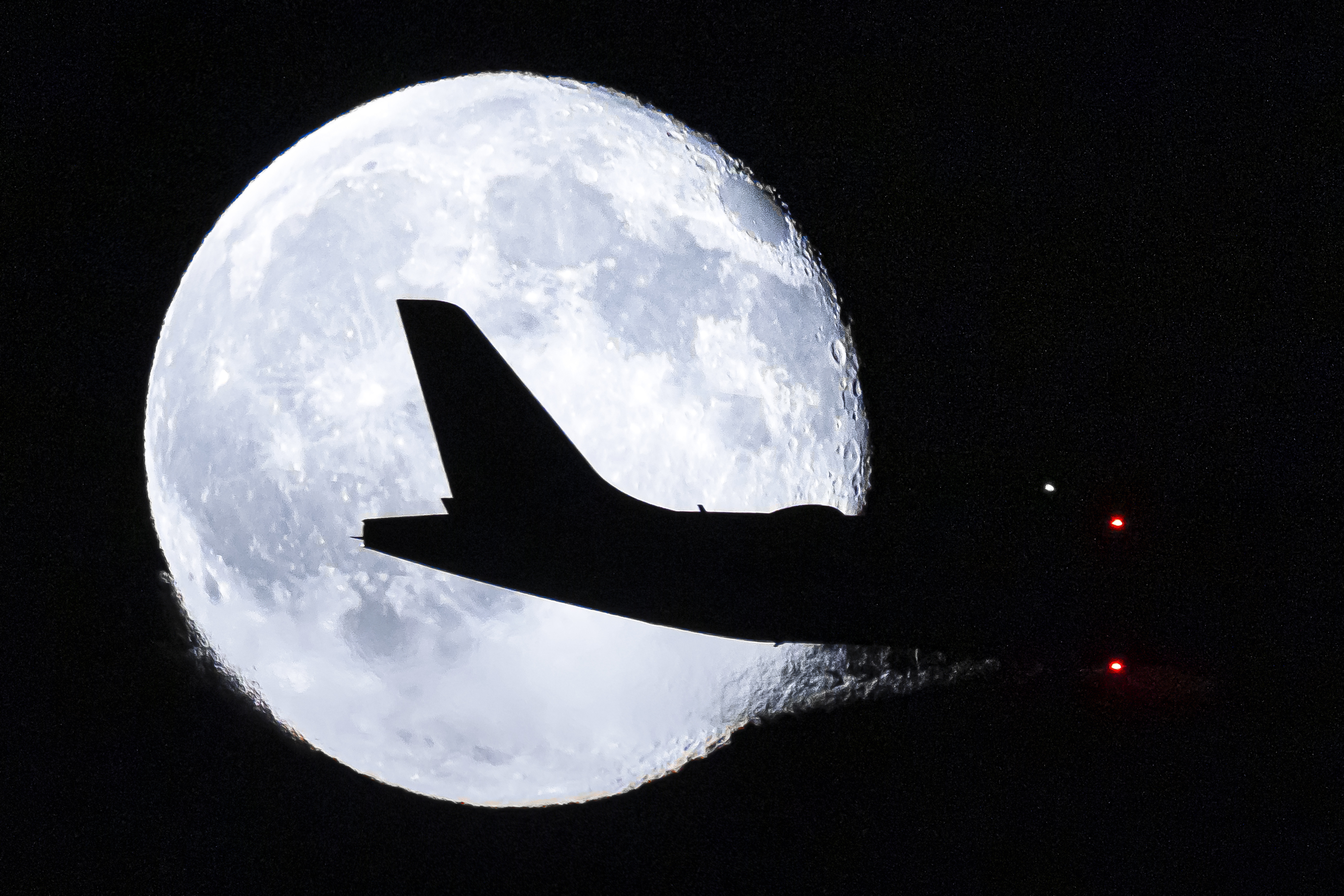 La silhouette di un aereo si staglia contro la luna piena durante il suo avvicinamento all'aeroporto di Zurigo.