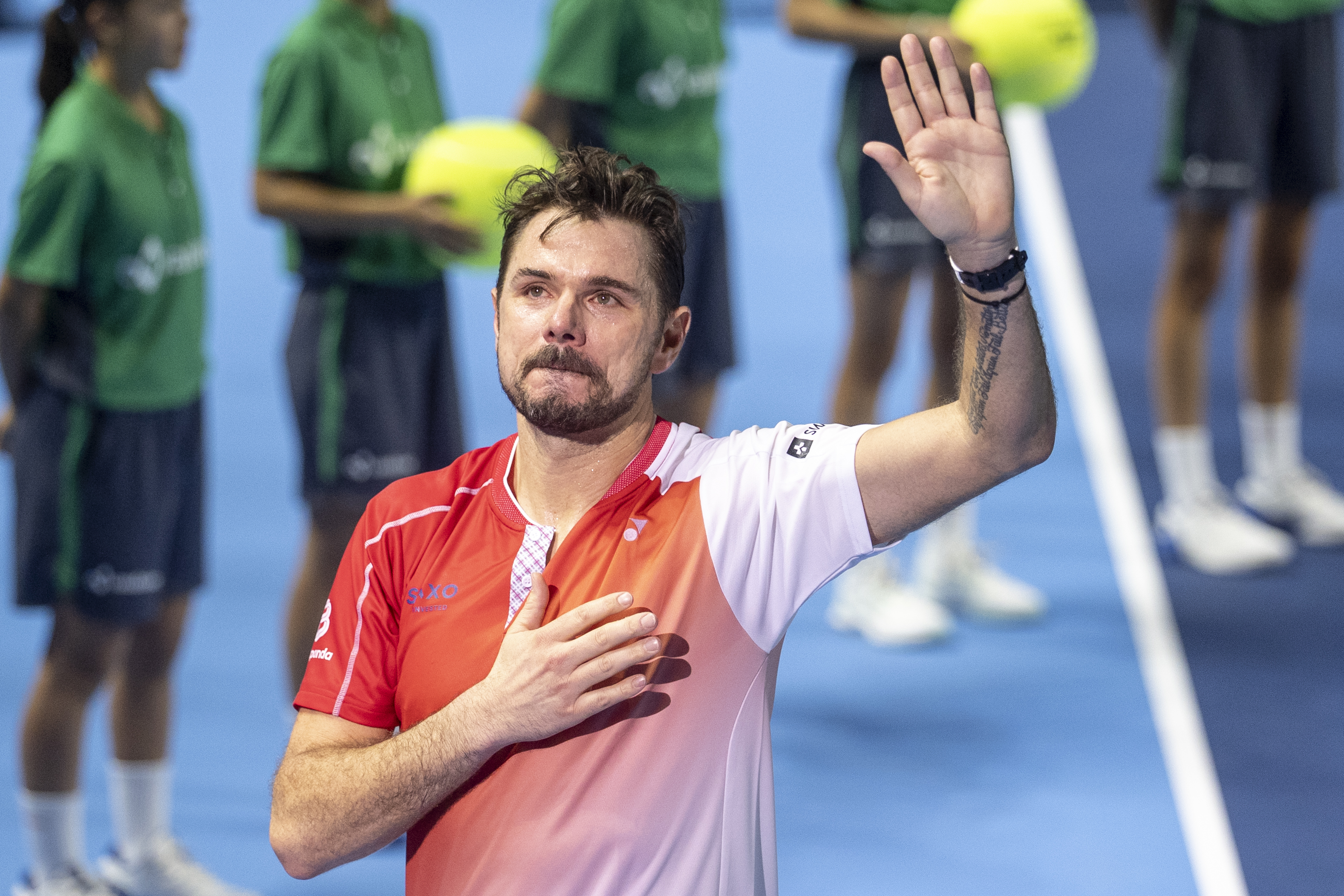 Ein Mann im Tennisdress auf einem Court, der sich ans Herz greift und mit der anderen Hand winkt