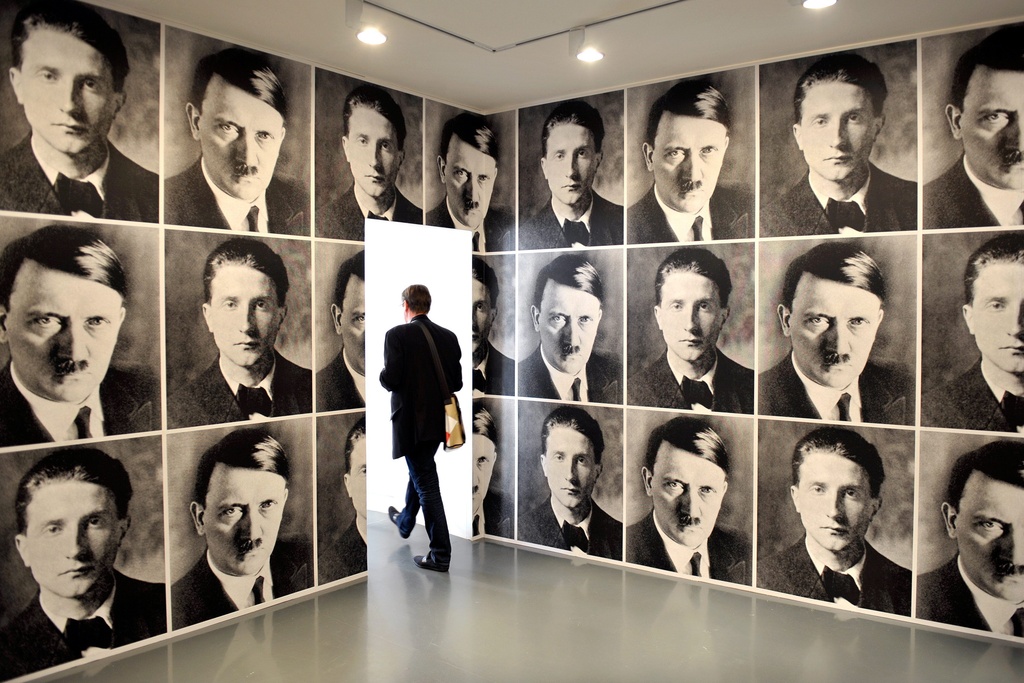 A man walks through a room at the Mudac decorated with wallpaper bearing  the images of Nazi leader Adolf Hitler and French artist Marcel Duchamp, by  German artist Rudolf Herz. - SWI
