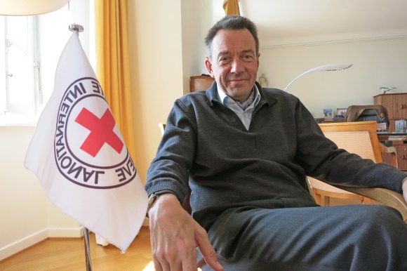 رجل يجلس وعلى يمينة علم اللجنة الدولية للصليب الأحمر