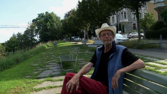 Un hombre mayor con un sombrero blanco de vaquero está sentado en un banco de un parque.