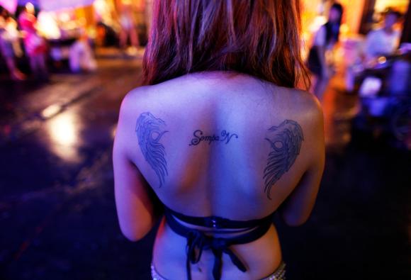 Eine thailändische Prostituierte von hinten fotografiert mit nacktem Rücken, auf dem mehrere Tattoos zu sehen sind.