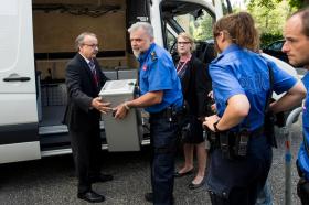 Agenti di polizia prendono in consegna le urne sigillate scaricate da un furgone bianco.