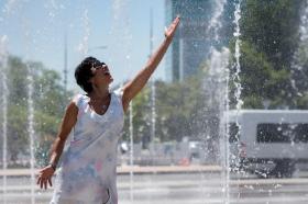 Frau kühlt sich unter einem Springbrunnen von der Hitze ab