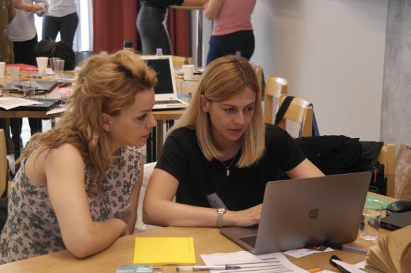 Zwei Frauen sitzen an einem Tisch vor einem Laptop.