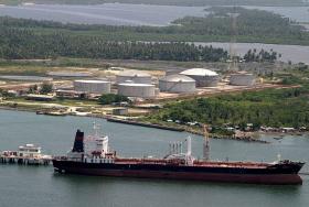 An oil tanker afloat in front of an oil facility situated amid trees