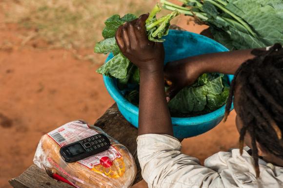 Une femme africaine lave des légumes à côté de son téléphone portable.