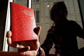L immagine illustra l ombra di una donna con un passaporto svizzero tra le mani.
