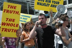 A man speaks into a megaphone amidst a crowd holding banners demanding truth