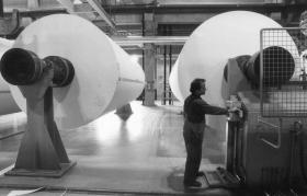 A worker attends to a giant roll of paper in a factory