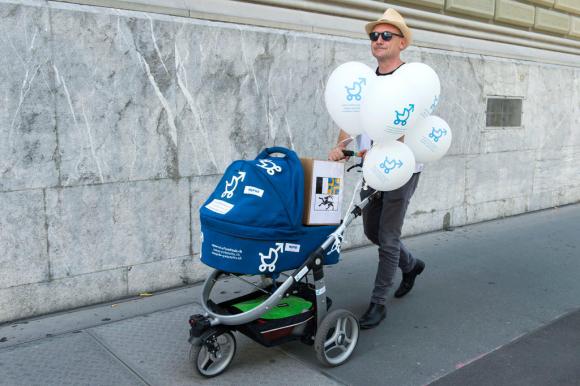 Ein Mann schiebt einen Kinderwagen, an dem Luftballons befestigt sind.