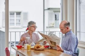 朝食をとりながら新聞を読む老夫婦の写真