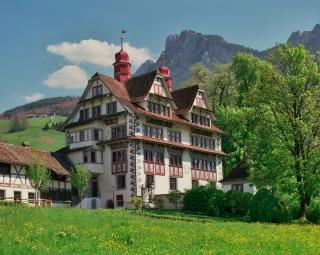 Weiss-rotes Gutshaus mit Zwiebeltürmchen in grüner Landschaft