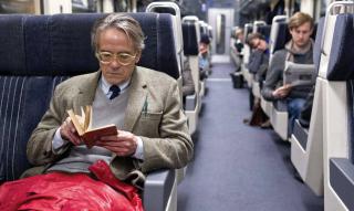 Un uomo seduto sul treno legge un libro.