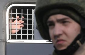 A prisoner s hand at the bars of a cage with a soldier in foreground