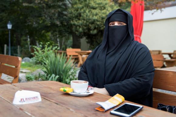 Eine voll verschleierte Frau sitzt vor einem Cappuccino