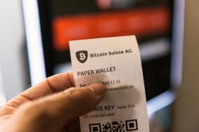 A hand holds a paper receipt for bitcoins
