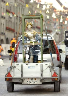 la statua della Giustizia è trasportata su un rimorchio trainato da un auto.