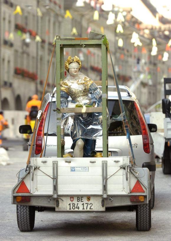 la statua della Giustizia è trasportata su un rimorchio trainato da un auto.