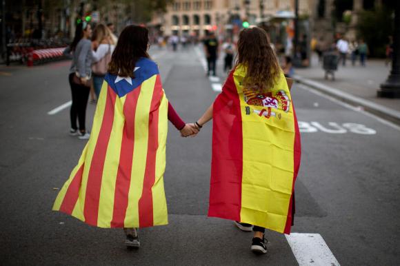 Dos jóvenes de espalda, una con la bandera española, otra con la estelada catalana, se dan la mano.