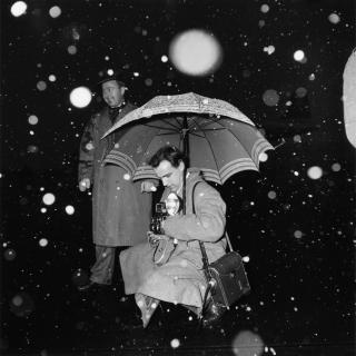 in Pressefotograf mit seiner Ausrüstung unter dem Regenschirm im Schneegestöber