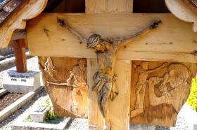 Ein helles Holzkreuz mit dem gekreuzigten Christus im Vordergrund.