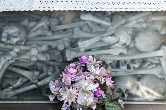 Knochen und Totenköpfe aufgeschichtet, davor ein Blumenstrauss