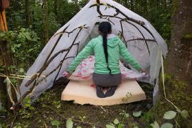 View of the back of a woman making a makeshift bed in a homemade tent in a forest area.