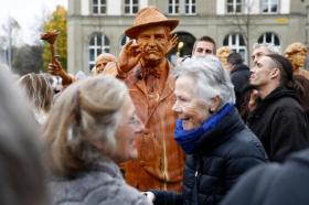 Una scultura in legno di Gottlieb Duttweiler esposta su una piazza e circondata di persone che la osservano