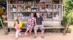 زوجان يجلسان على مقعد أمام كشك في الفلبين بينما تلعب ابنتهم بجوارهما