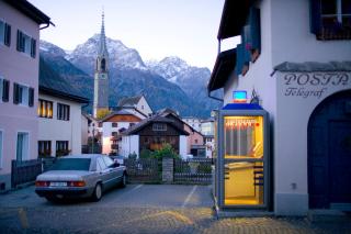 cabina telefonica illuminata in un villaggio e sullo sfondo le montagne innevate