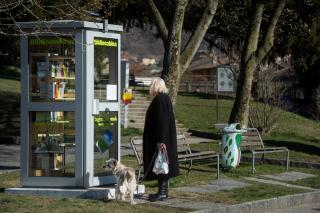 donna col cane legge un annuncio affisso sulla porta di una cabina trasformata in biblioteca