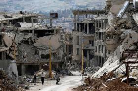 ثلاثة أشخاص وسط أطلال مدينة سورية تعرضت للقصف