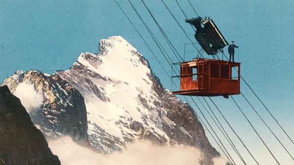man standing on cable car going up mountain