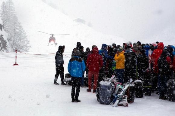 雪の中、ヘリコプターの到着を待つ観光客