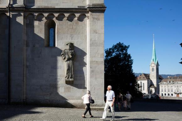 passanti davanti al duomo di Zurigo, dove su una parete esterna c è la statua del riformatore Heinrich Bullinger.