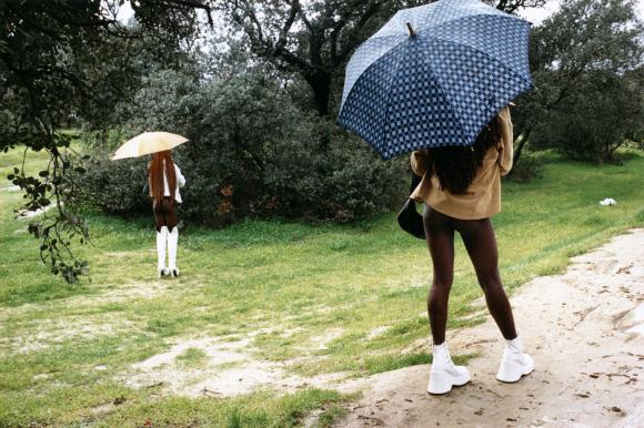 Zwei Prostituierte aus Nigeria stehen mit offenen Regenschirmen im Grünen.
