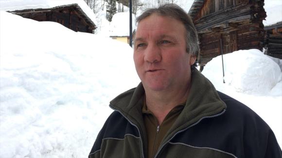 Ein Mann steht vor einem Holzhaus, umgeben von viel Schnee.