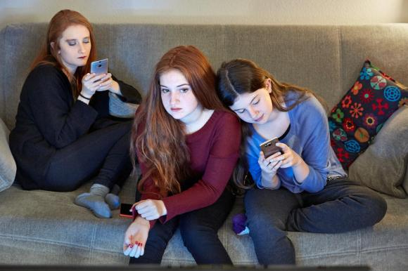 A picture of three girls on a sofa staring at their phone