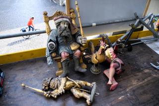 Figures of Chronos, a lion and Joker lie on the scaffold floor, Below a cyclist drives by.