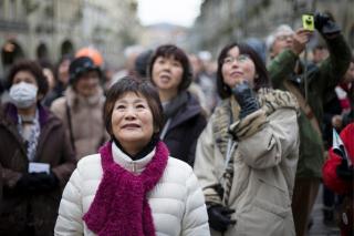 Japanese people, standing outside, dressed in winter coats, looking upwards.