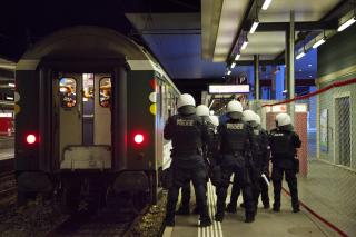 Gruppo di sette agenti in tenuta antisommossa, di schiena, accanto alla coda del treno