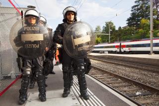 Due agenti in tenuta anti-sommossa accanto ai binari; in lontananza, un treno