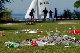 Pile of rubbish on grass in front of a lake and sailing boats