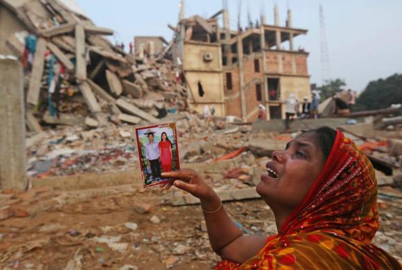 Davanti alle macerie dell edificio crollato, una donna piange mostrando la foto di una coppia.