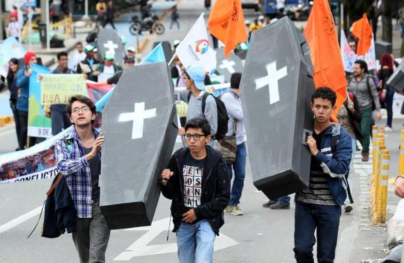 Drei junge Männer tragen an einer Demonstration zwei schwarze Särge